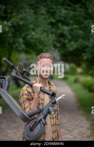 Buon umore. Uomo in camicia a scacchi con il suo scooter e sorridente Foto Stock