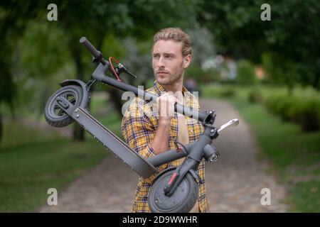 Nel parco. Uomo in camicia a scacchi con il suo scooter e girandosi Foto Stock