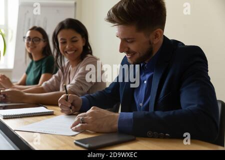 Felice giovane impiegato maschio che firma il contratto di lavoro che viene assunto Foto Stock