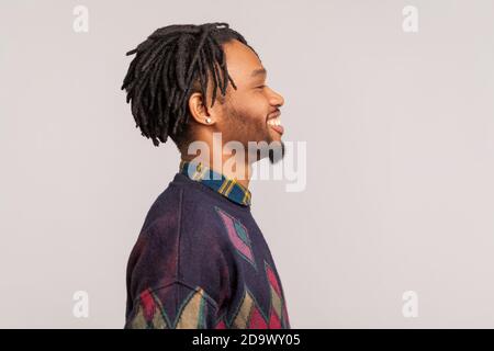 Profilo ritratto uomo africano estremamente felice con dreadlock guardando avanti con sorriso toothy, ottimismo, successo. Studio interno isolato su grigio b Foto Stock