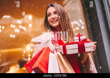 Felice giovane donna attraente con borse di carta e scatole di regalo in mani dopo lo shopping di Natale nel centro commerciale. Allegra bella ragazza tenere borse e shopping Foto Stock