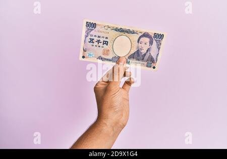 Mano ispanica con una banconota da 5000 yen giapponese su sfondo rosa isolato. Foto Stock