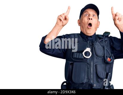 Uomo anziano bello che indossa uniforme della polizia stupito e sorpreso guardando in su e puntando con le dita e le braccia sollevate. Foto Stock