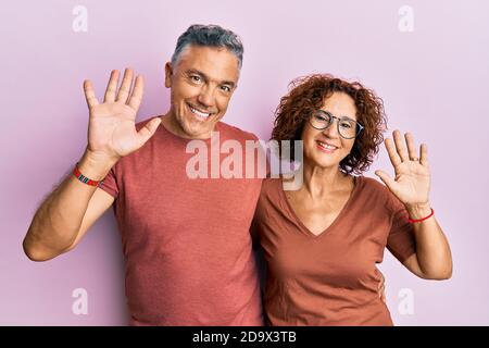 Bella coppia di mezza età insieme indossare abiti casual cintura dicendo ciao felice e sorridente, amichevole gesto di benvenuto Foto Stock