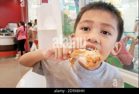 Carino ragazzo asiatico mangiare pollo fritto è delizioso. Foto Stock