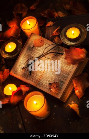 Un vecchio libro con gli occhiali da lettura illuminati da candele e. decorato con foglie d'autunno Foto Stock