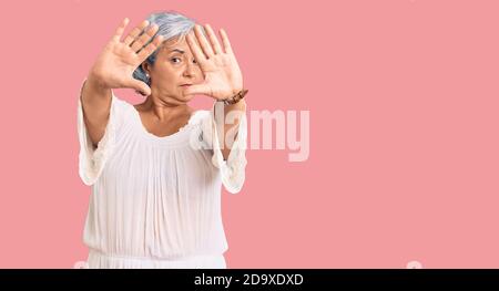 Donna anziana con capelli grigi che indossano stile bohémien che fa cornice usando le mani palme e le dita, prospettiva della fotocamera Foto Stock