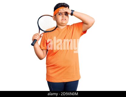 Ragazzino che gioca a tennis tenendo la racchetta stressata e frustrata con la mano sulla testa, sorpresa e faccia arrabbiata Foto Stock