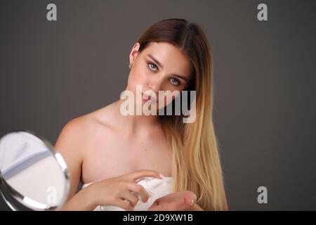 bellezza, cura del corpo e concetto della gente - bella giovane donna che applica lo spray o la nebbia facciale alla sua pelle del viso su sfondo grigio Foto Stock