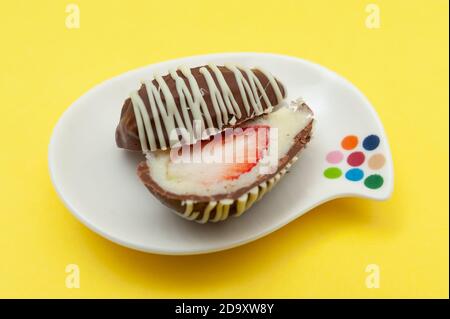 Uovo di cioccolato (uovo di Pasqua) cocco farcito con fragola tagliata a metà su un piatto. Isolato su sfondo giallo. Primo piano. Foto Stock