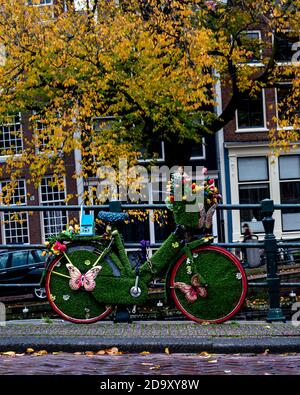 Bicicletta decorata con colori colorati parcheggiata contro una ringhiera di una Amsterdam ponte di canale con sullo sfondo un albero di colore giallo foglie Foto Stock