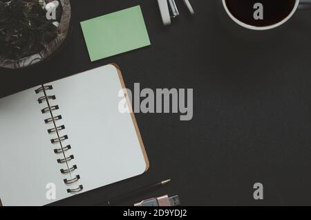 Scrivania da ufficio con blocco note, caffè, foglia e penna su sfondo nero. Spazio per la copia vista dall'alto. Tonalità vintage Foto Stock