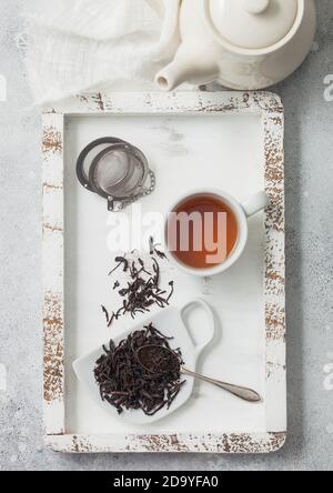 Tè nero sciolto con infusore di tisane e teiera in ceramica con tazza in scatola di legno con panno di lino bianco. Vista dall'alto Foto Stock