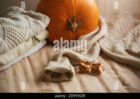 Accanto ai pullover bianchi caldi e morbidi, una grande zucca arancione e una foglia di acero secca sono impilati in un mucchio. Preparazione per la stagione autunnale. Decorazione per Foto Stock