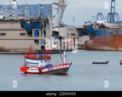 Tradizionale barca da pesca in legno ancorata di fronte ad un grande cantiere navale a Laem Chabang, il più importante porto commerciale della Thailandia. Foto Stock