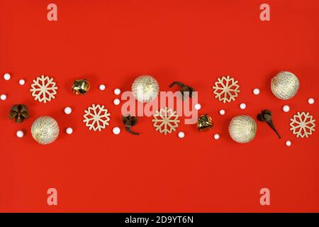 Piatto di Natale con ornamenti in legno fiocco di neve, campane dorate e palle e baubles ornamento albero che formano linea in mezzo a sfondo rosso Foto Stock