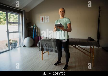 Foto a tutto corpo di una fisioterapista femminile che naviga su un tablet digitale in piedi nella palestra. Foto Stock