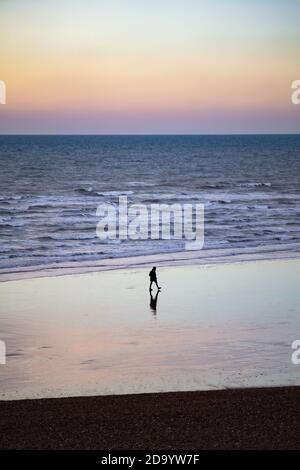 Una singola figura che prende una passeggiata di mattina presto lungo Hastings spiaggia Foto Stock