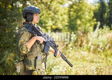 forte e coraggiosa soldato militare con fucile mitragliatrice in piedi nella foresta, è pronta a sparare al nemico, armi da fuoco campo di tiro all'aperto Foto Stock