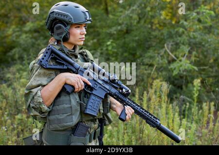 coraggiosa donna caucasica è impegnata in armi da caccia pistola o fucile, indossando tuta militare. bersaglio sparato. cacciatrice femminile in foresta selvaggia, natura. caccia di successo. caccia sport concetto Foto Stock