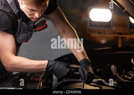 riparando in action. dipendente del tipo hardworking in uniforme lavora nel salone dell'automobile, meccanico sicuro dell'automobile è lavoratore professionale di servizio Foto Stock