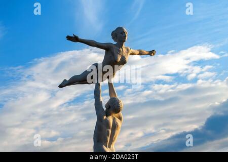 Scultura sovietica del parco fatta di vetroresina, l'uomo tiene la donna sopra la testa contro il cielo blu con le nuvole. Foto Stock