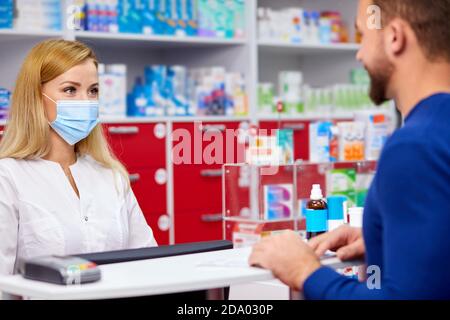 giovane professionista dract dare farmaci al cliente in farmacia moderna, consultare e raccomandare, indossare maschera medica di protezione dal coronavirus covid-19 Foto Stock