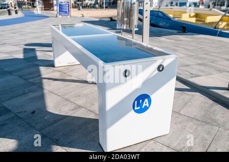 Panca con pannello solare e caricabatterie mobile sul lungomare di la Ampolla, Tarragona, Catalogna, Spagna Foto Stock