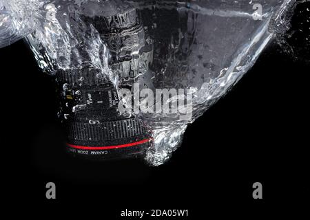 L'obiettivo della fotocamera DSLR si tuffa nell'acqua su uno sfondo nero Foto Stock