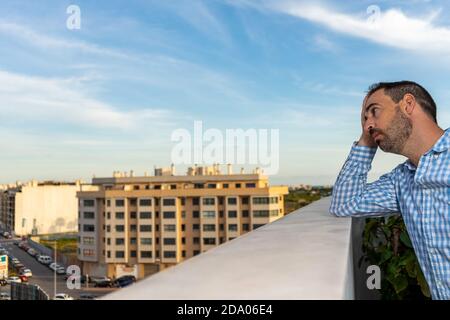 Giovane attraente, triste e disperato uomo ispanico che soffre di depressione che sembra pensieroso e frustrato sulla terrazza della sua casa guardando depr Foto Stock