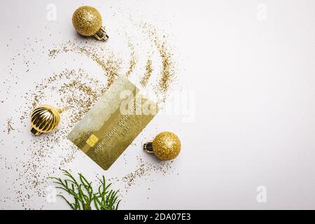 Concetto di shopping di natale in linea con le palle di natale, la polvere dorata e mockup della carta di credito dorata su sfondo bianco. Vista dall'alto, disposizione piatta Foto Stock