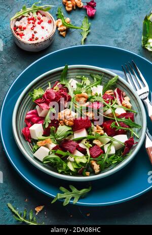 Insalata estiva di barbabietole con rucola, radicchio, formaggio morbido e noci su piatto con forchetta, condimento e spezie su tavolo da cucina blu, spazio copia, vista dall'alto Foto Stock