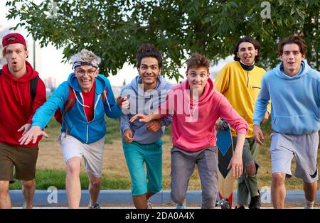 ritratto di allegri ragazzi caucasici all'aperto, giovani ragazzi in coloratissimi abbigliamento casual corrono in avanti, sorridono. squadra felice Foto Stock