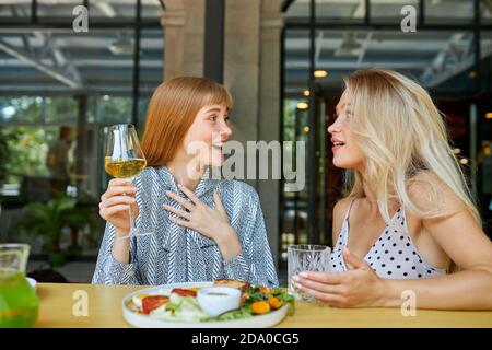 due donne caucasiche positive amano trascorrere il tempo insieme al ristorante, le donne bionde parlano e bevono bevande, gustano il pasto. non si vedono a lungo Foto Stock