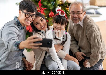 Famiglia asiatica multigenerazionale, mamma papà figlia ragazza e nonno, selfie Con un albero di Natale dopo decorare l'ornamento di Natale preparare mari Foto Stock