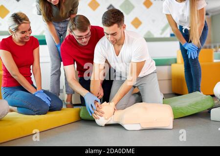 Classe CPR con giovani istruttori caucasici che parlano e dimostrano aiuto al primo soccorso, manichino cpr sul pavimento Foto Stock