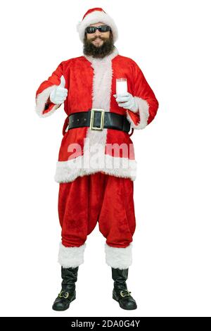 Il Babbo Natale arabo con la barba nera tiene il bicchiere del latte, mostra il pollice verso l'alto. Babbo Natale tiene un bicchiere di latte su sfondo bianco. Natale in arrivo Foto Stock