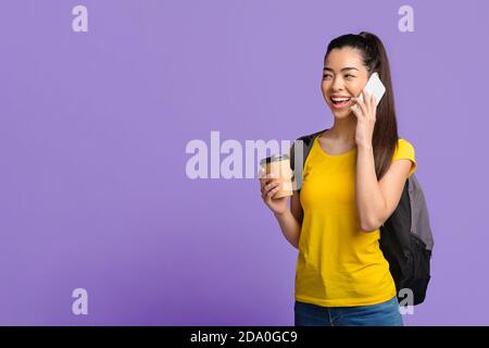 Allievo femminile asiatico allegro con zaino che parla su Cellphone e. Bere caffè Foto Stock