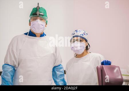 Stomatologo maschile irriconoscibile con collaboratore femminile in maschere respiratorie e. occhiali protettivi che guardano la fotocamera al lavoro Foto Stock