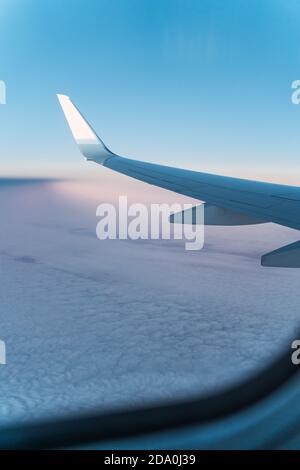 Vista dell'ala bianca dei moderni aerei che volano all'alba su nuvole contro il cielo blu Foto Stock