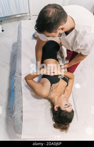 Alto angolo di fisioterapista maschile che fa massaggio di loin per paziente femminile sdraiato sul tavolo in sala medica durante la riabilitazione processo Foto Stock