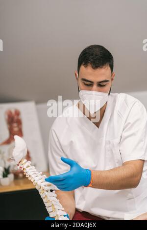 Fisioterapista maschile che spiega la struttura della colonna vertebrale per la paziente femminile durante l'uso modello in plastica e seduta in sala medica durante la sessione di riabilitazione Foto Stock