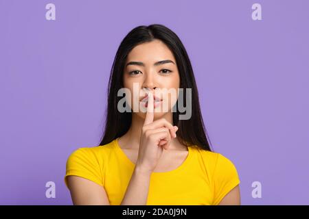 Shhh. Misteriosa giovane donna asiatica che mostra mantenere il segno del silenzio alla macchina fotografica Foto Stock