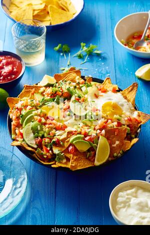 Chilaquiles - colazione messicana fatta di fagioli neri, mais, patatine di tortilla e uova fritte su tavolo di legno blu Foto Stock