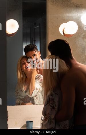 Bell'uomo bearded abbracciando allegra ragazza mentre sfregava i denti insieme in bagno al mattino Foto Stock