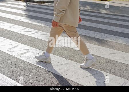Pedone maschile tagliato irriconoscibile che indossa abiti casual traversata su zebra attraversate la strada il giorno di sole Foto Stock