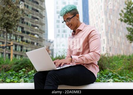 Vista laterale basso angolo di felice imprenditore africano americano maschio lavorare al progetto mentre si è seduti con un computer portatile per strada Foto Stock