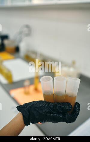 Irriconoscibile scienziato di raccolto in guanto di lattice in piedi in laboratorio con raccolta di provette con liquido chimico giallo Foto Stock