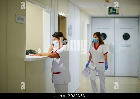 Personale medico irriconoscibile che parla al telefono vicino al partner femminile in camminare in modo uniforme nel corridoio dell'ospedale con carta Foto Stock