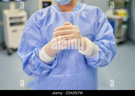 Anonimo femmina medic in maschera sterile e guanti guardando fotocamera in ospedale dietro l'apparecchiatura medica Foto Stock